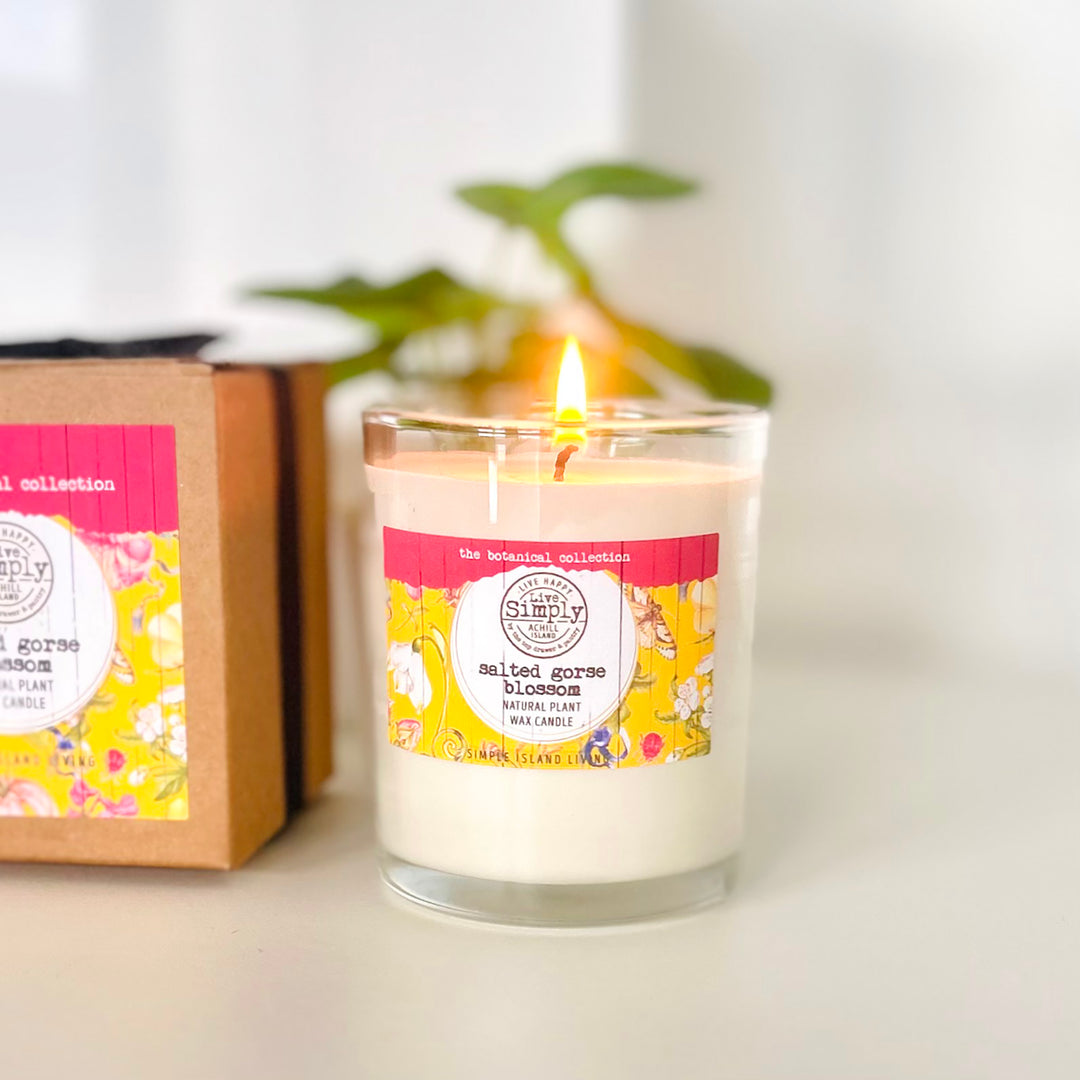 Candle with a floral label next to a cardboard box on a white surface