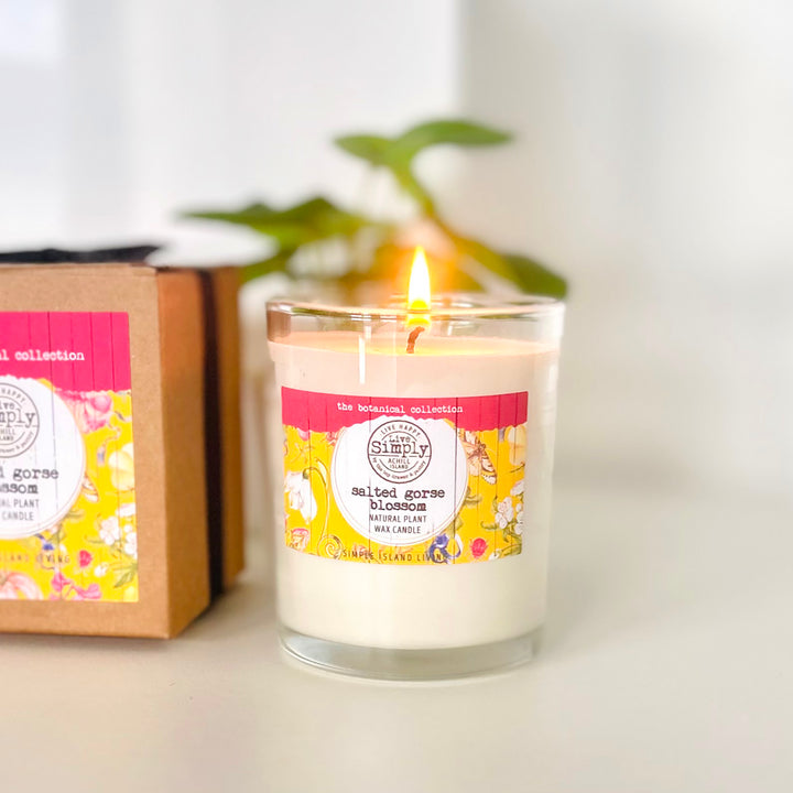 Candle with a floral label next to a cardboard box on a white surface