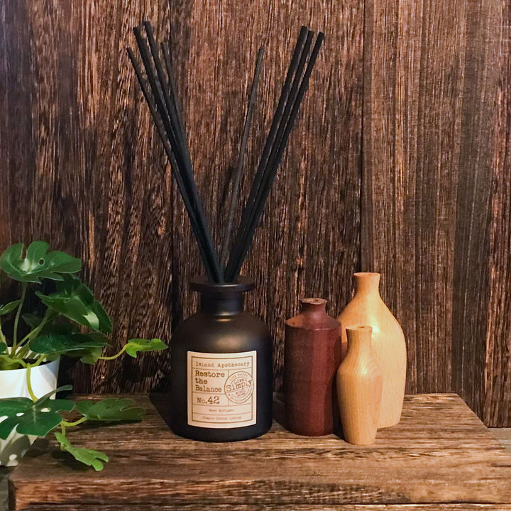 Black diffuser with reeds on a wooden surface with decorative vases and plants.